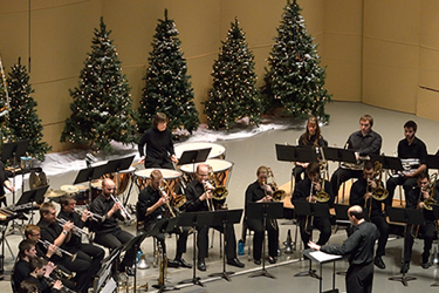 A brass ensemble, accompanied by percussion, performs on stage. There are Christmas trees on stage behind the musicians.