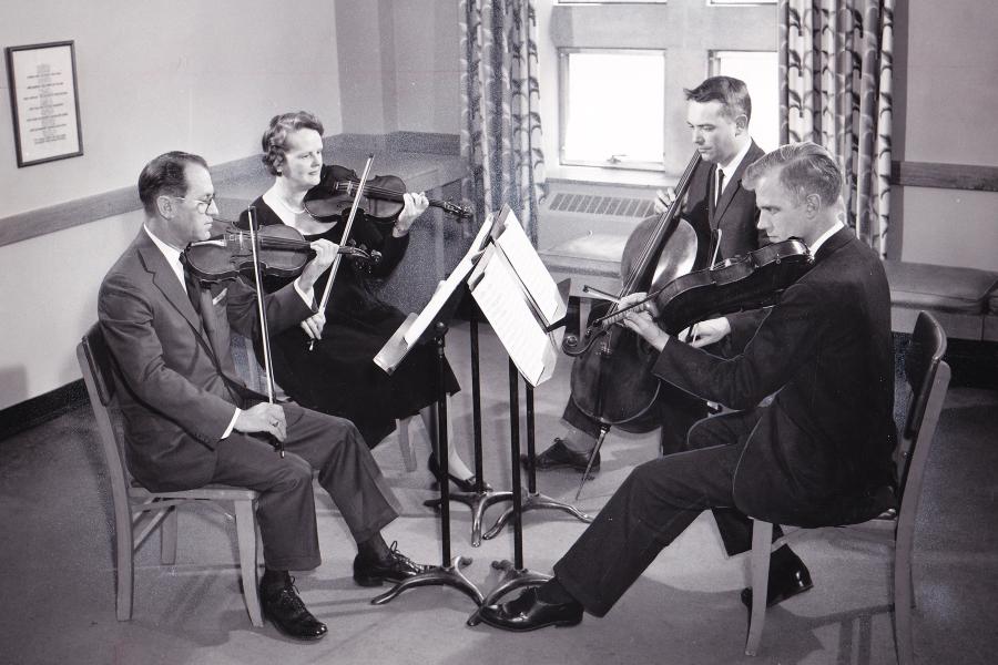 A black and white photo of a string quartet rehearsing in a small room.