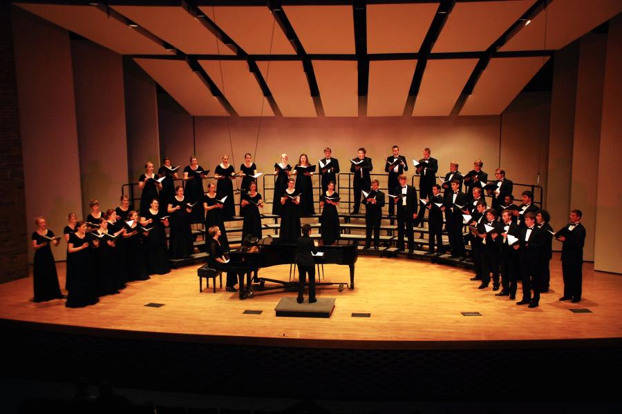 A choir performing on stage, accompanied by a pianist.