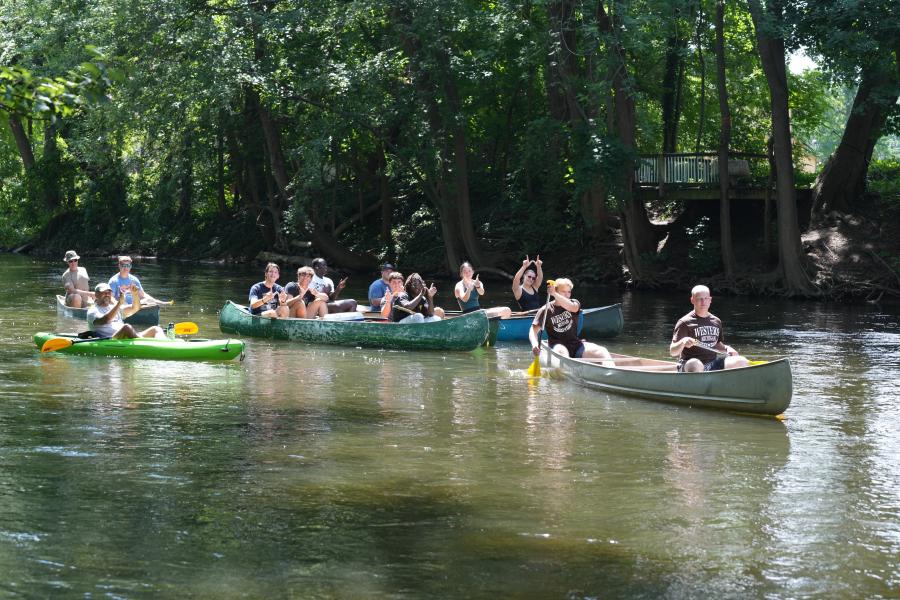 Students paddle down the Kalamazoo River on kayaks and canoes.