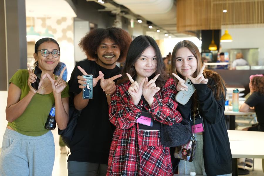 Four students facing the camera with a smile and making the W sign.