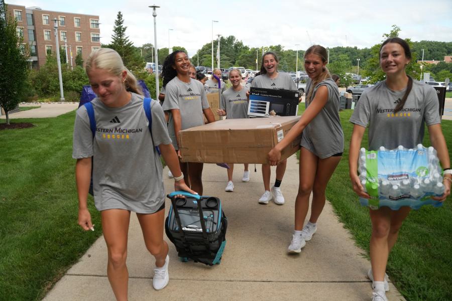 Members of the women's soccer team carry belongings into a residence hall.