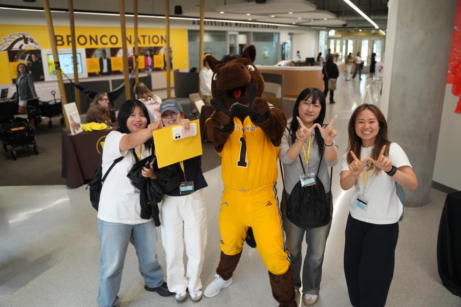 Buster Bronco takes a photo with students.
