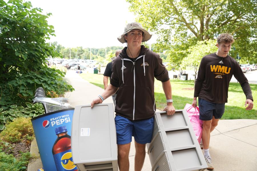 Students carry belongings into a residence hall.