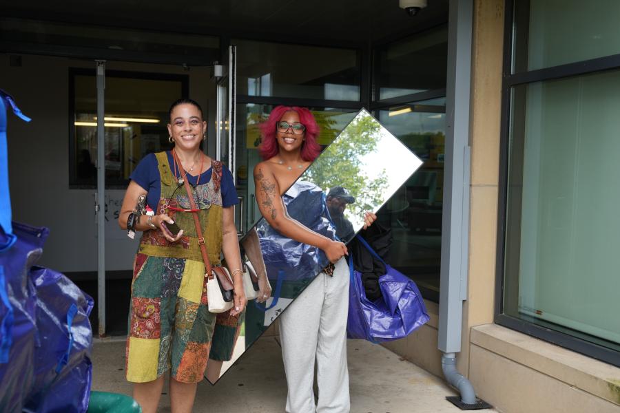 Two people carry belongings into a residence hall.