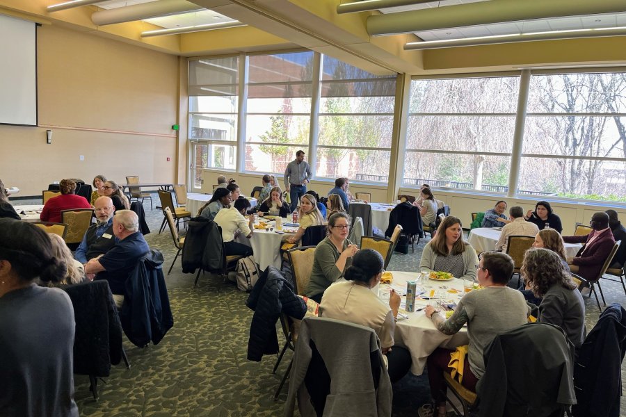 A group of people sitting at round tables chatting before an Evaluation Cafe
