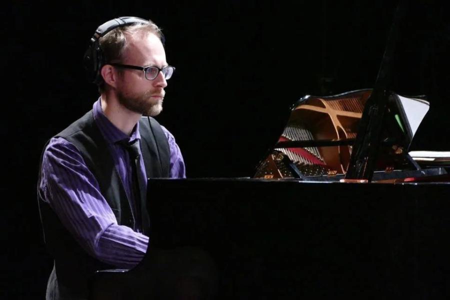 A man in a purple shirt and black vest playing the piano.