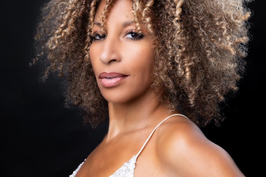 A light-skinned woman with curly hair wearing a sleeveless white top. 