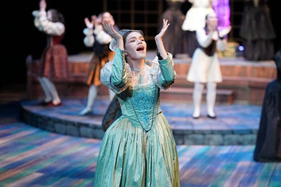 A female opera singer in an ornate blue dress, performing on stage.