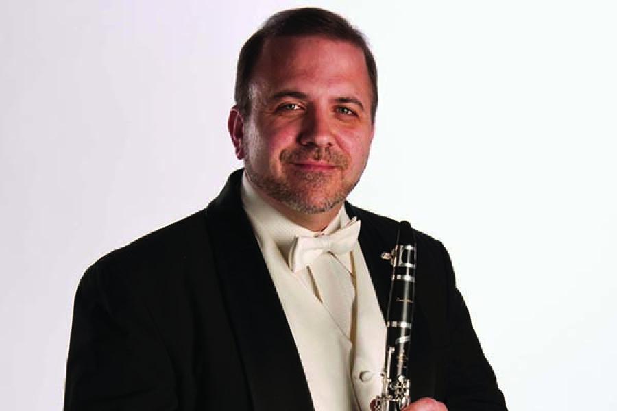Smiling man in a tuxedo holding a clarinet.