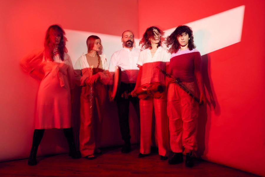 Five musicians holding instruments, standing in a line under a red light. 