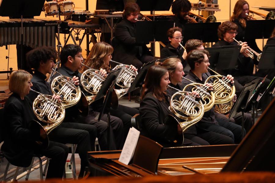 The horn section of a concert band performing on stage.
