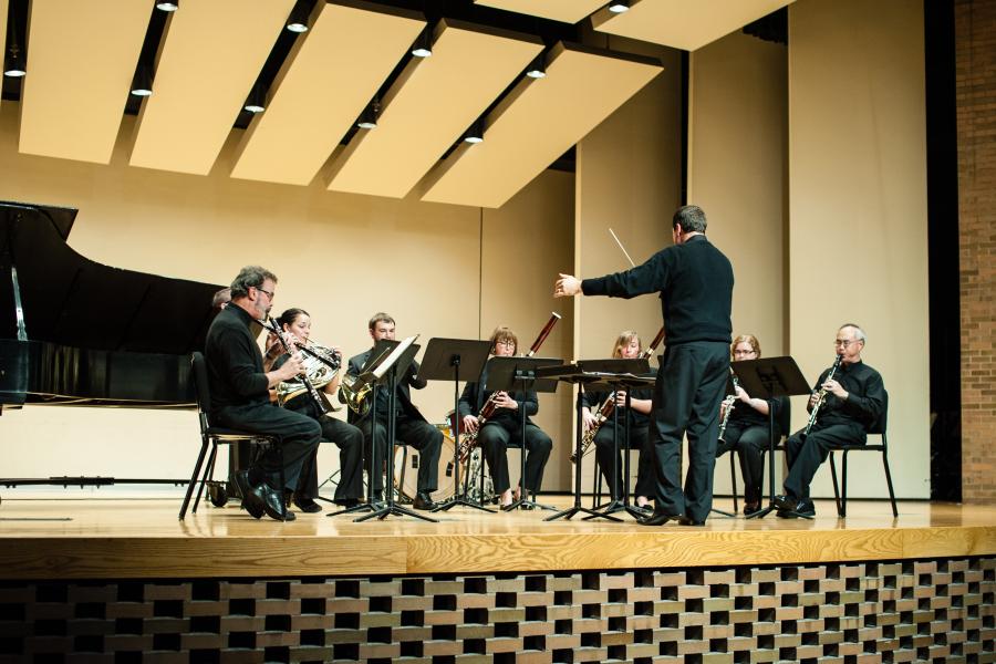 A chamber octet consisting of oboes, French horns, bassoons, and clarinets (two of each instrument) performing on stage, conducted by Scott Boerma.