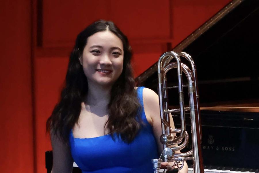 A smiling woman wearing a blue dress holding a bass trombone.