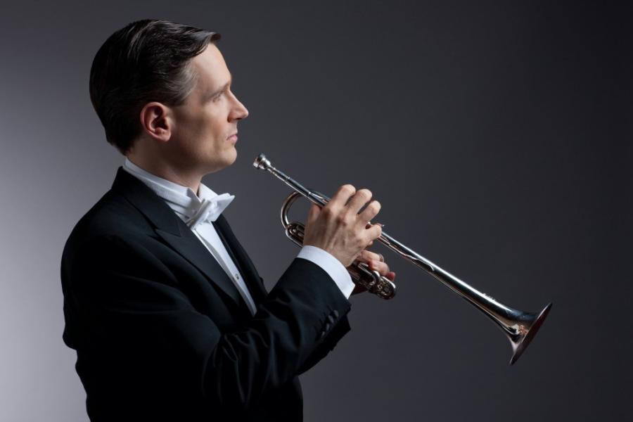 A man in a black and white tuxedo holding a silver trumpet.