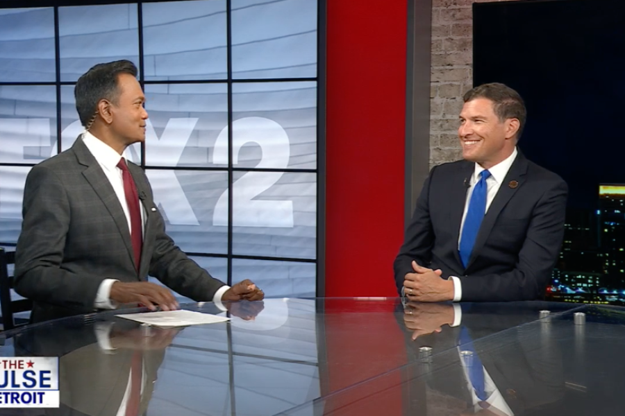 President Russ Kavalhuna sits at a news desk with a news anchor.