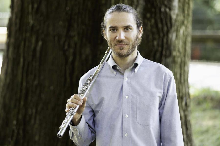 A smiling man wearing a blue button-down shirt, holding a flute.