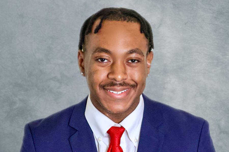 Headshot of Michael Harmon in a blue suit with a red tie on a grey background