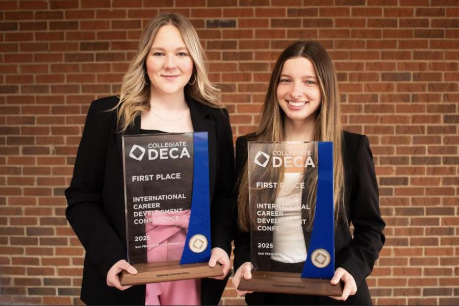 Two students holding the DECA First Place trophy.