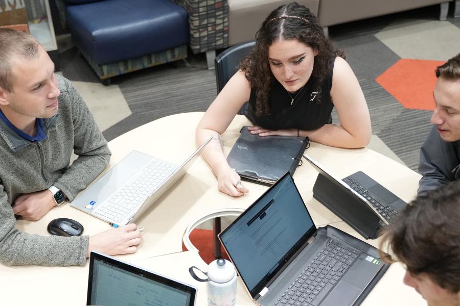Students with laptops and backpacks working at table.