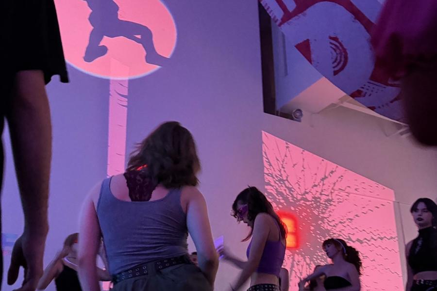 Many students dancing in the student art gallery with banners and projection around them.