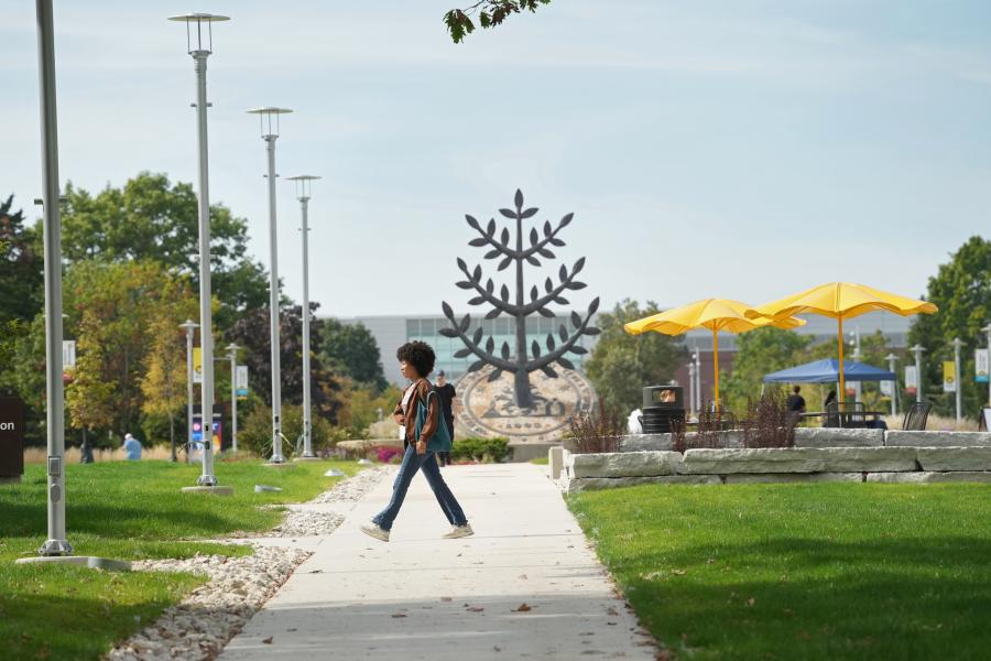 A student walking across campus in front of the Tree of Life statue.