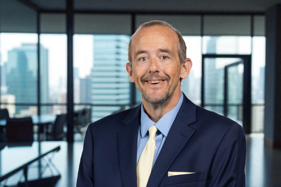 Headshot of Michael Andres in a suit with a yellow tie with an office background