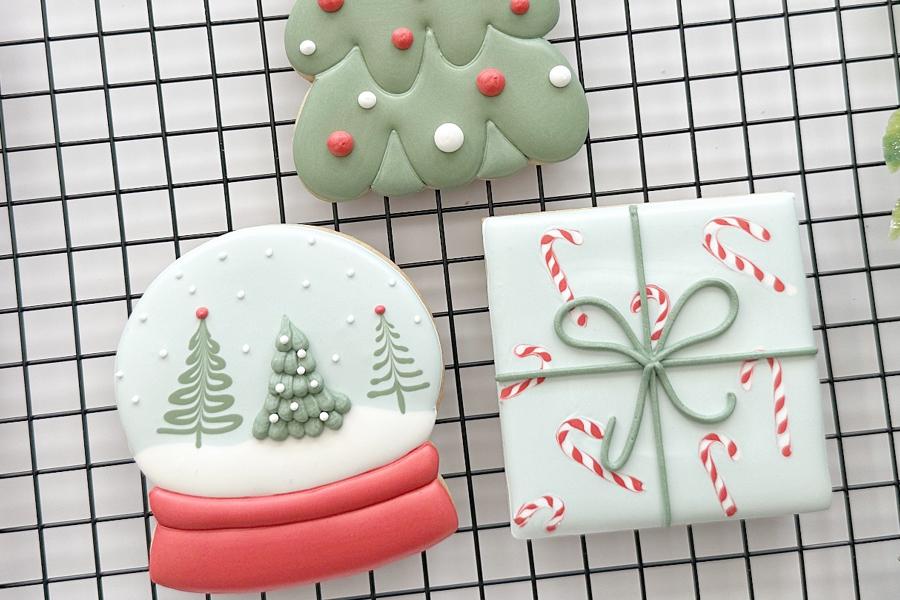 close up of three holiday cookies, a globe, gift and tree.