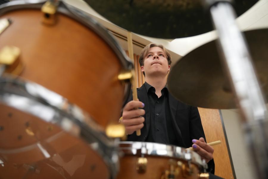 A musician in a black suit plays the drum set in a jazz ensemble.