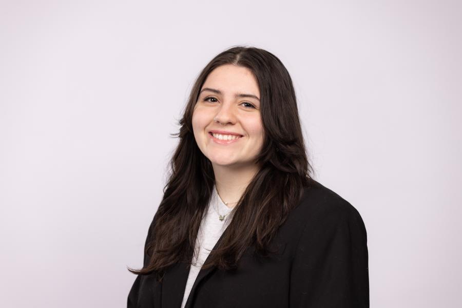 Headshot of Leena Shrum in a black blazer on an off-white background.
