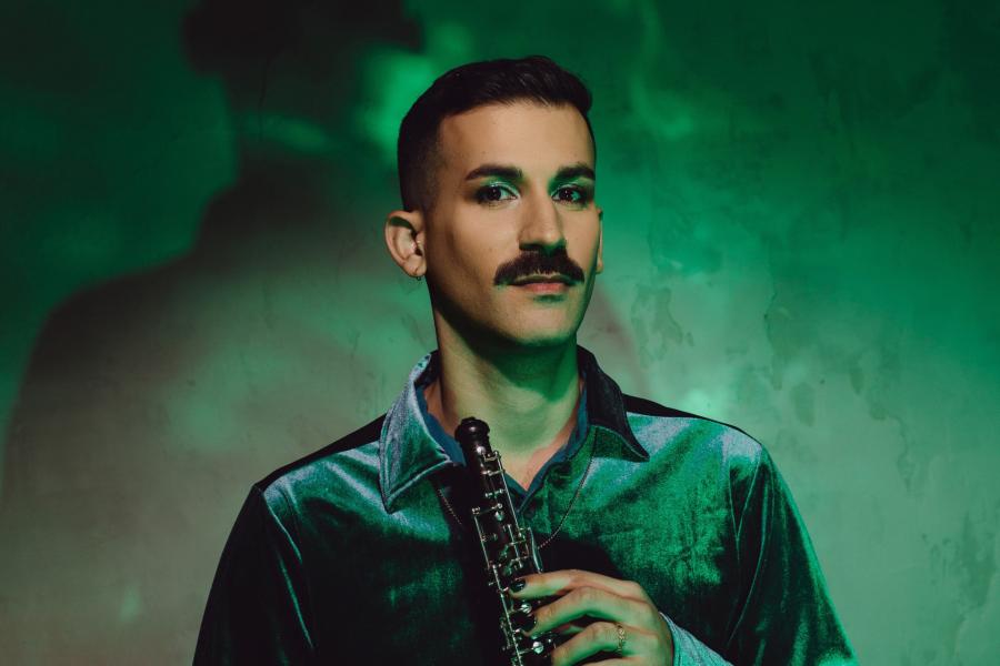 A person wearing a green shirt, with green eyeshadow, in a room with green walls, holds an oboe.