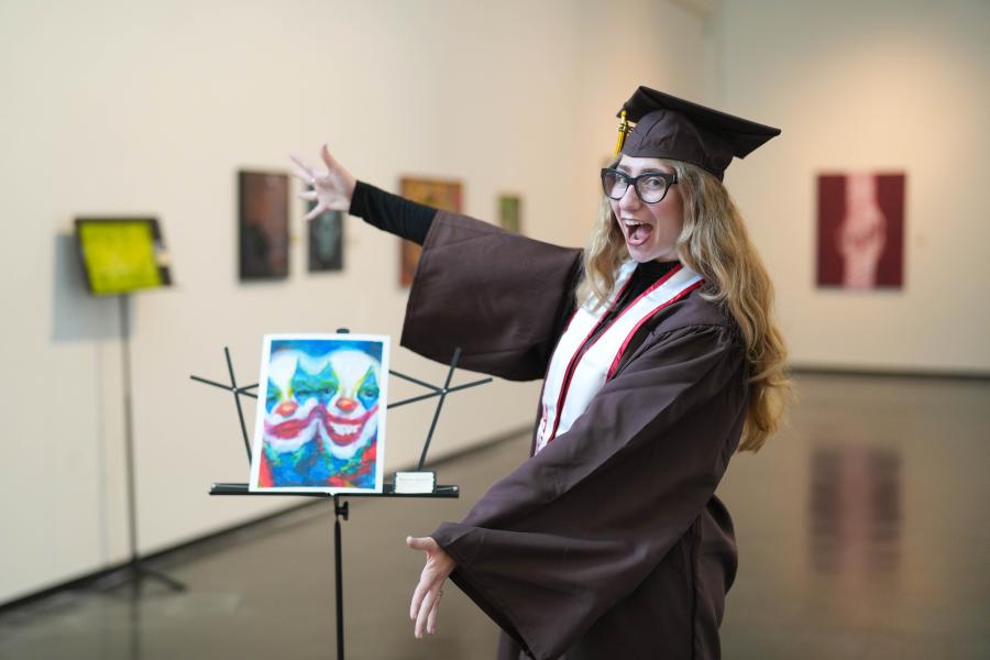 Hope Donovan, dressed in graduation regalia, shows off her painting.