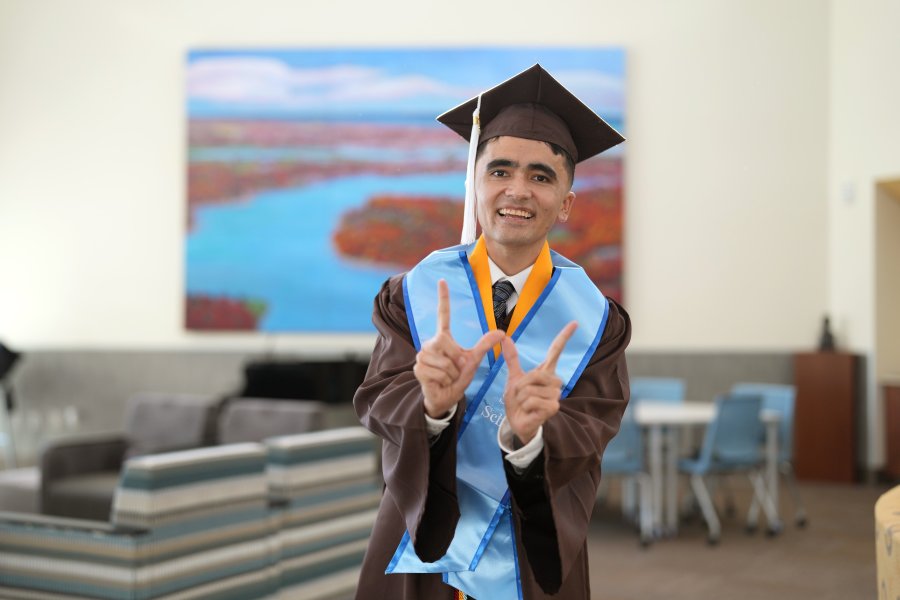 A portrait of Mehran Najafi in his graduation regalia holding up a W sign with his hands.