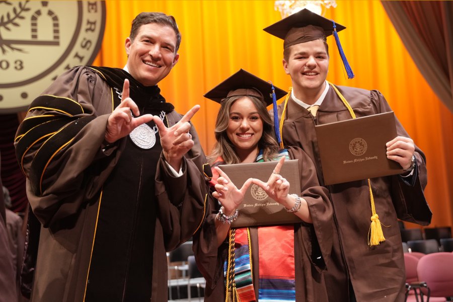 President Russ Kavalhuna, Daniela Padilla and Miles Cramer pose for a photo in graduation regalia.