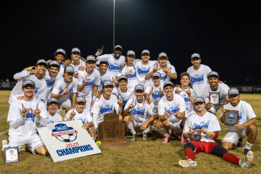 A group photo of the men's soccer team with a trophy.