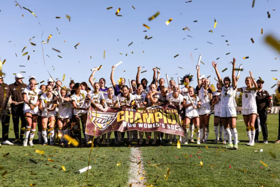 A group photo of the women's soccer team with a trophy.