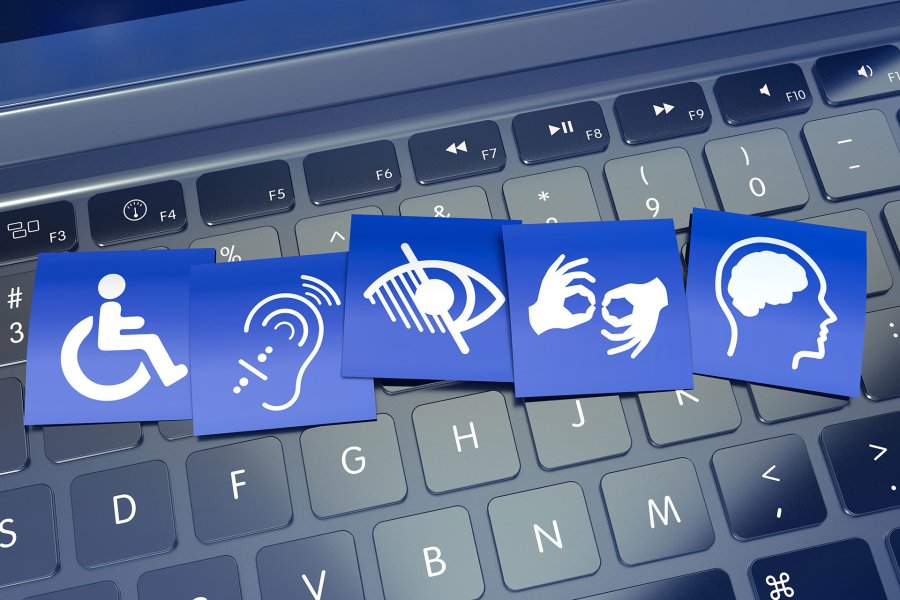 A computer keyboard with small printed sheets displaying accessibility icons, such as a wheelchair symbol and screen reader icon, placed on top.