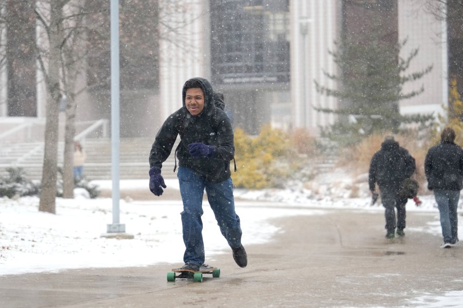 a student longboards on campus on a snowy day