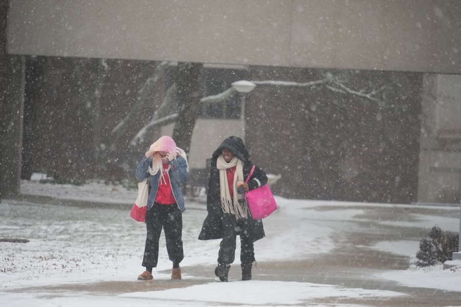 two students walk through snow falling down on campus