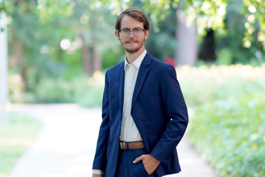 A man in a blue suit and glasses stands outdoors.