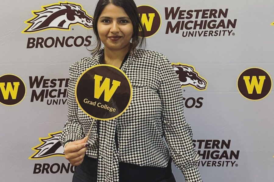 International student from India, Trivedi, stands for photo with WMU wall. 