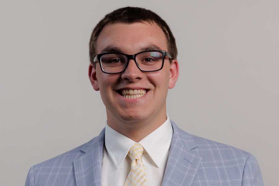 Headshot of Landon Wiedenhoeft in a grey suit with a yellow tie on a white background