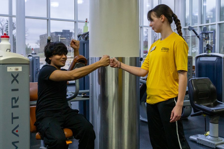 Personal trainer fist bumping with a client who is sitting and working out on a machine. 