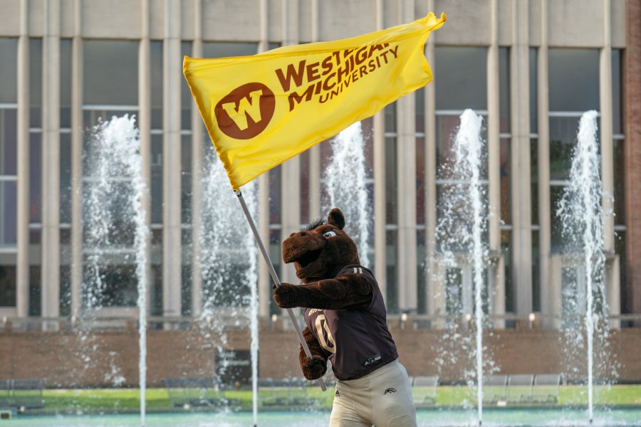 WMU mascot Buster waving WMU flag by fountain