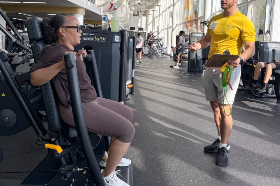 Participant in the weight room with a personal trainer making sure they are working out correctly.