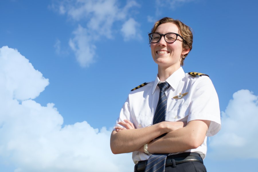 A Western Michigan University student posing in pilot gear in front of a blue sky.