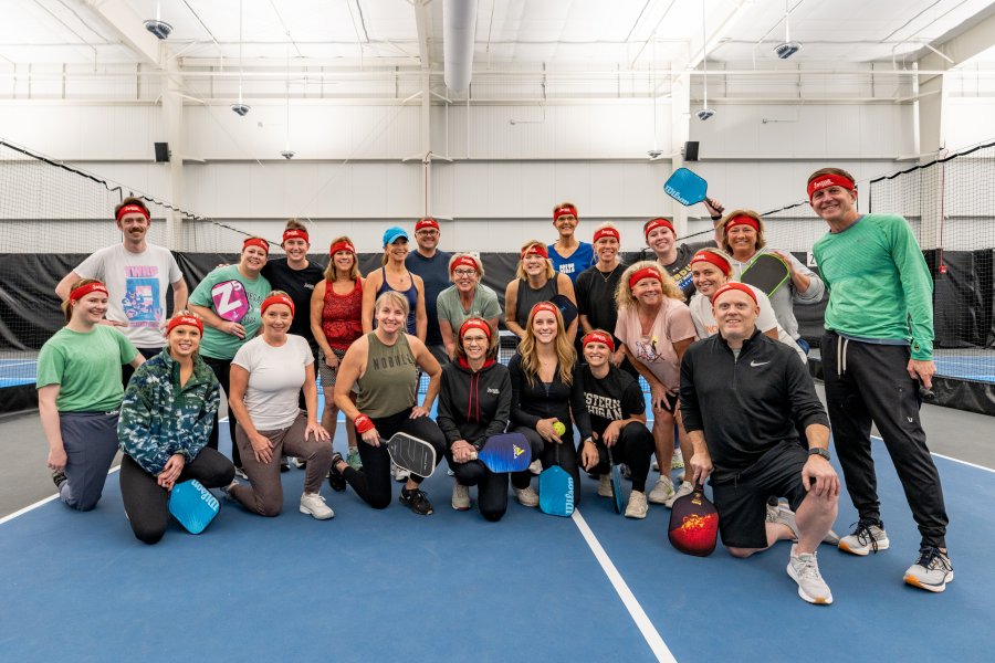 A group photo in front of the pickleball net at a corporate event.