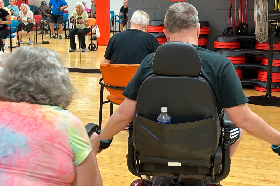 a man in his fourties duing arm raises weights as he sits in a wheelchair.