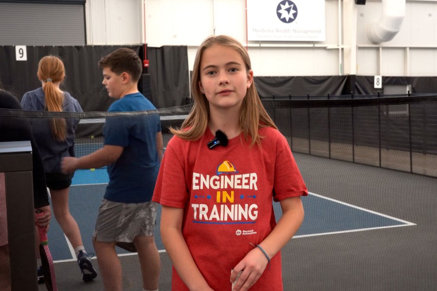 10 year old girl in a red tshirt standing in front of a pickleball court.