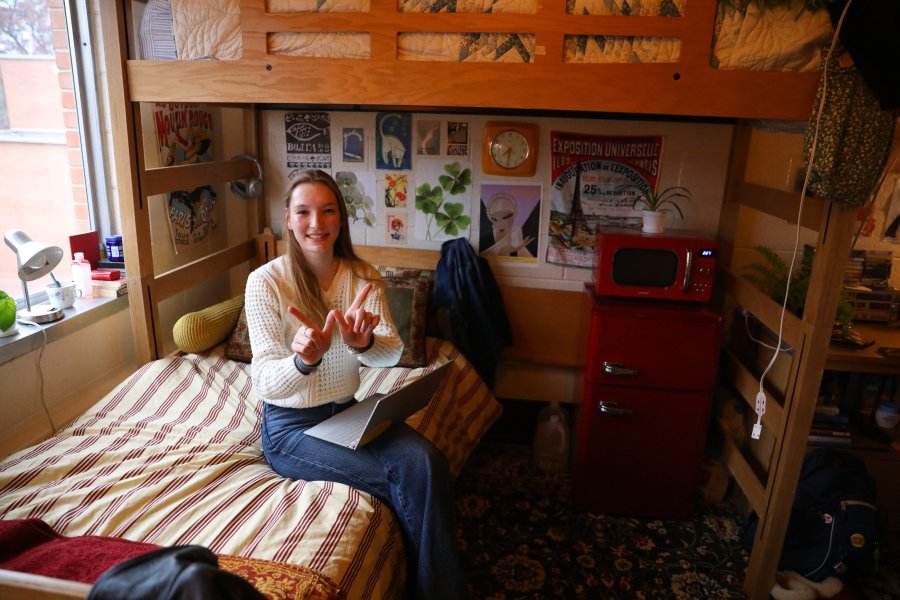 A student sits on the lower bunkbed in a decorated residence hall room.